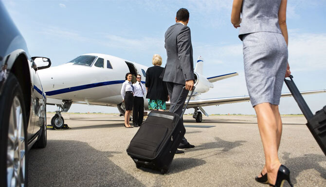 Business man and woman with rolling suitcases after exiting a limo at a an FBO airport about to enter a private plane. Boston Chauffeur FBO executive corporate limo service.